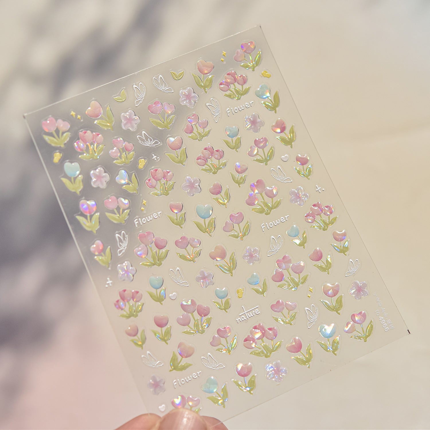 Sheet of floral and butterfly stickers held by a hand on a neutral background