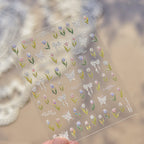 Sheet of decorative stickers with flowers, butterflies, and ribbons held against a blurred background.