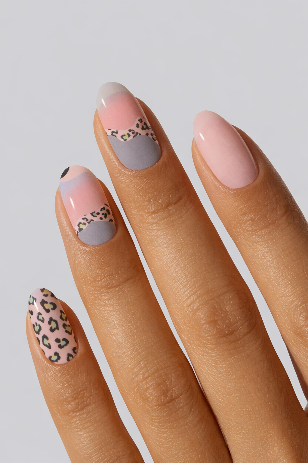 Hand with pink and gray nail wrap featuring leopard print designs n a light gray background