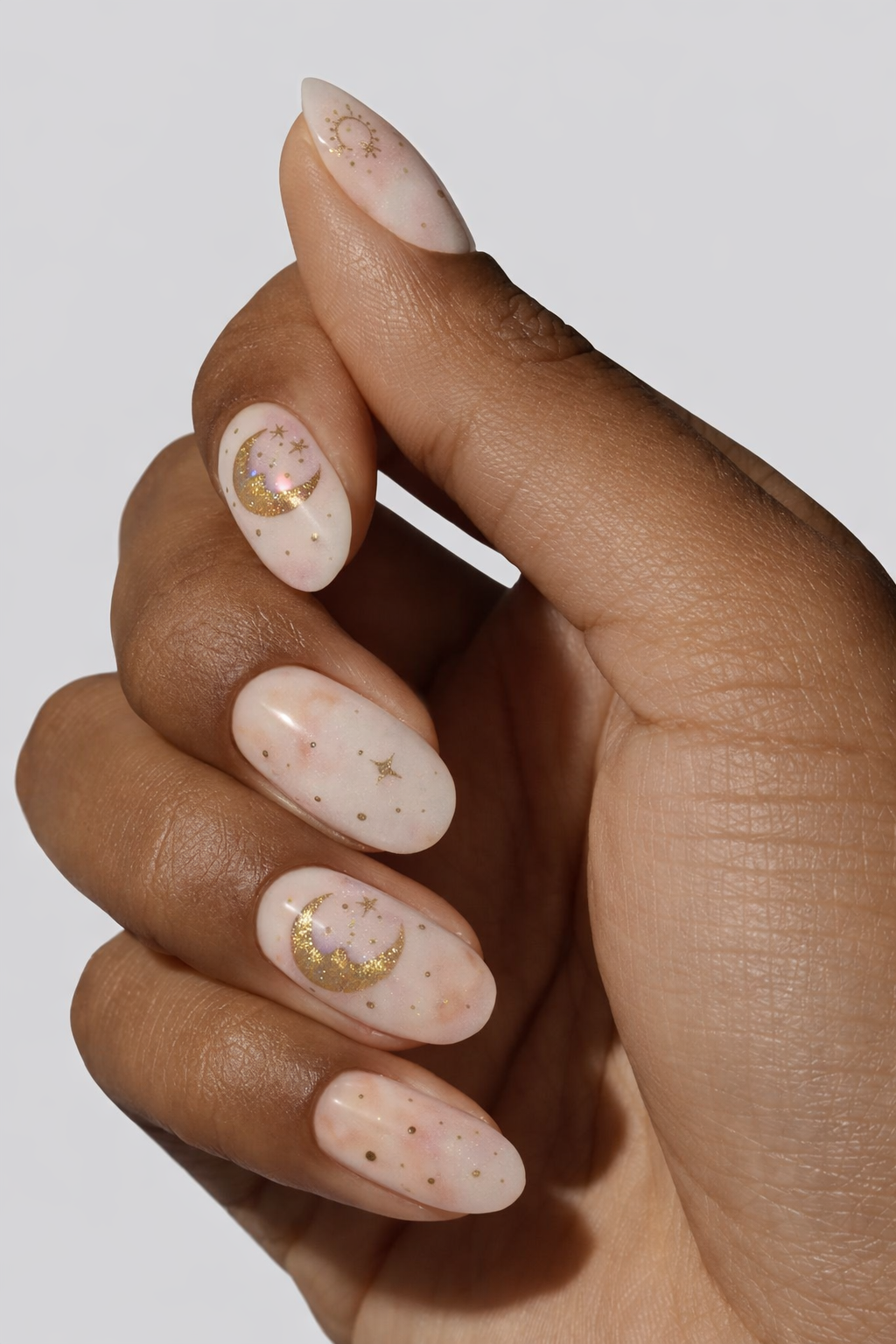 “Close-up of hand with nude nails decorated with small gold moon and star designs”