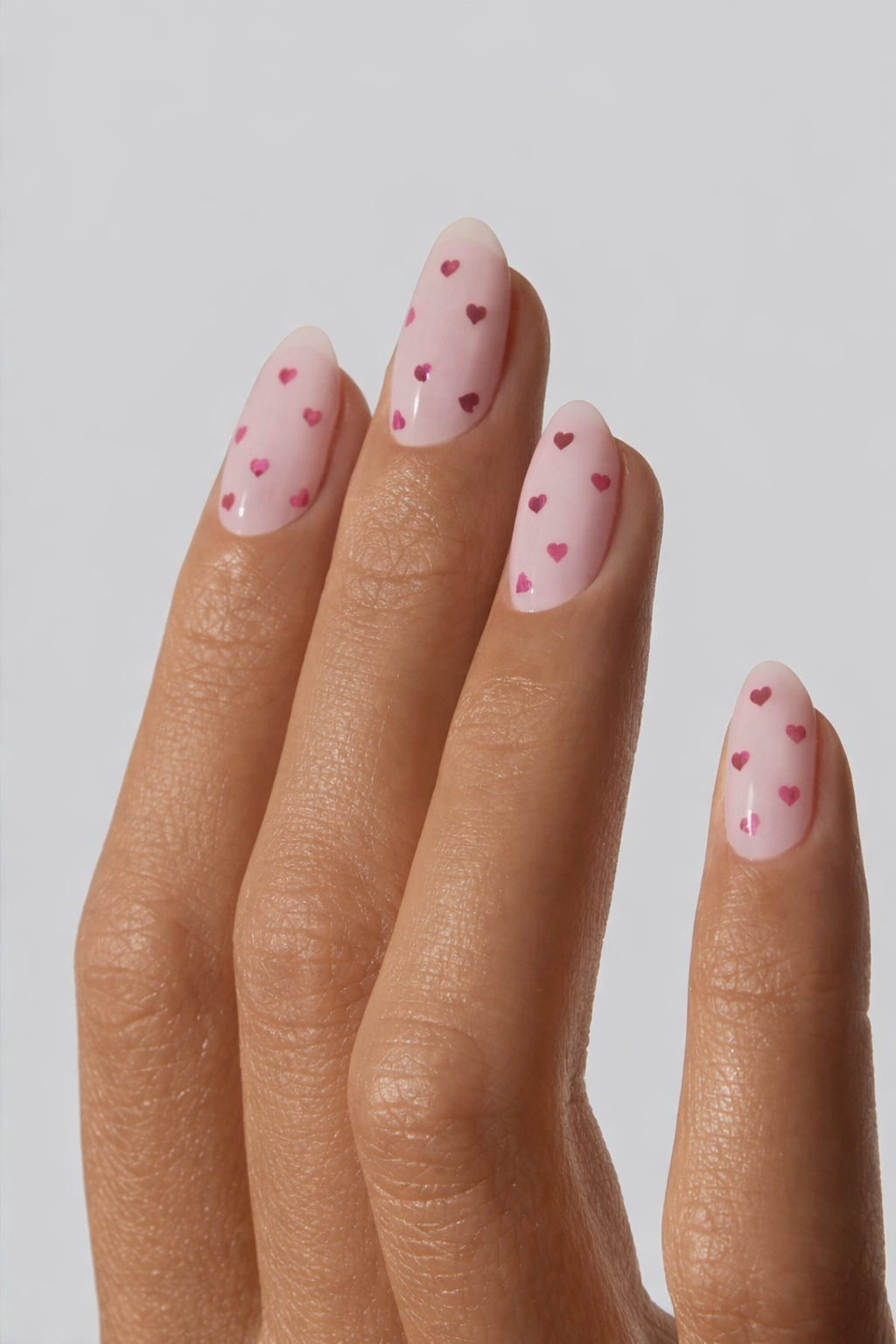 Hand with pink nail wrap featuring heart designs on a plain background