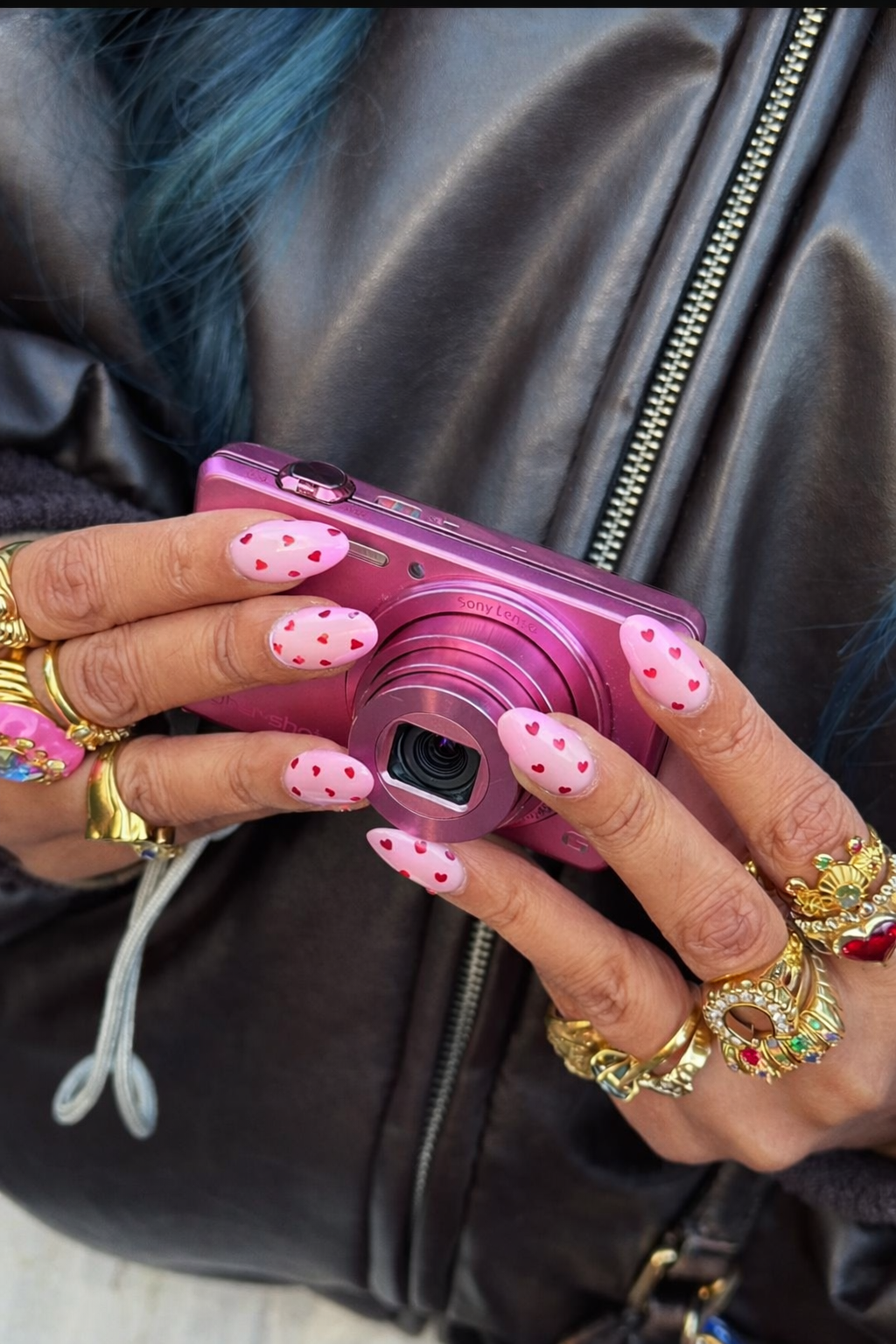 “Pink heart manicure nail wraps styled while holding a pink camera, close-up lifestyle shot”