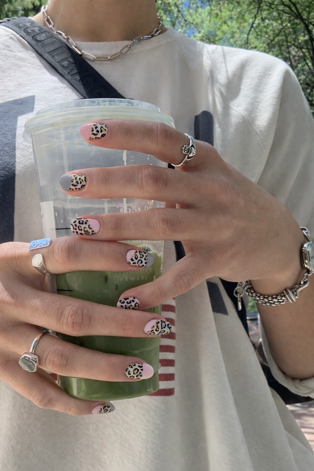 Hand holding iced matcha drink with pink leopard print YOUGLO nail wraps in outdoor setting