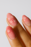 Peach pink manicure with small white flower designs and subtle glitter gradient.