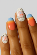 Close-up of hand with orange to blue gradient nails and speckled abstract accent designs
