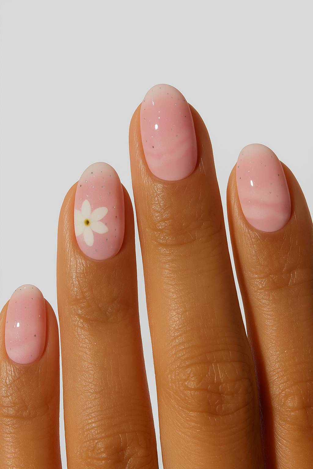 Soft pink ombre nail wraps with small white flower accent on hand”
