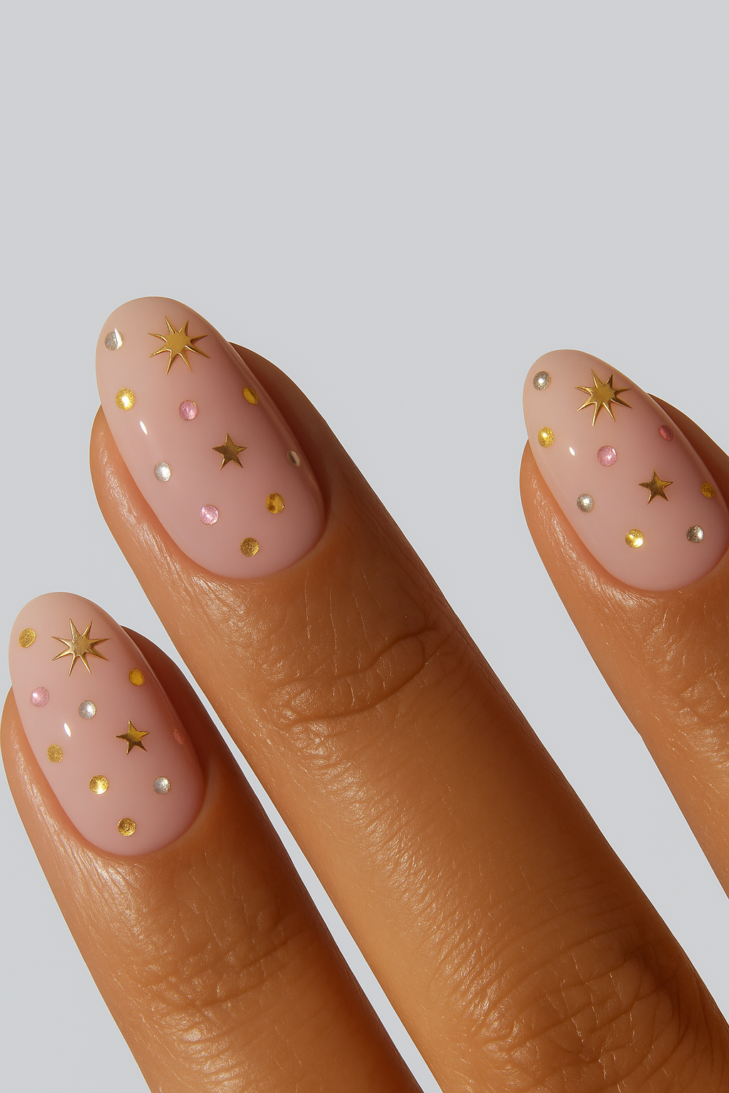 Nude nail wrap manicure with gold stars and subtle embellishments.