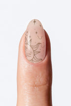Sheer nude nail wrap manicure with delicate sun and star art.