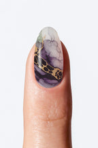 Nail with marbled design featuring purple, gold, and white on a neutral background