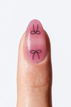 Pink gradient nail wrap with black bow design”