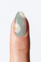 A fingernail with a green ombré nail wrap featuring flower design at the tip.