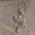 “Pink 3D butterfly nail art stickers shown with decorated sample nails featuring rhinestones and floral details.”