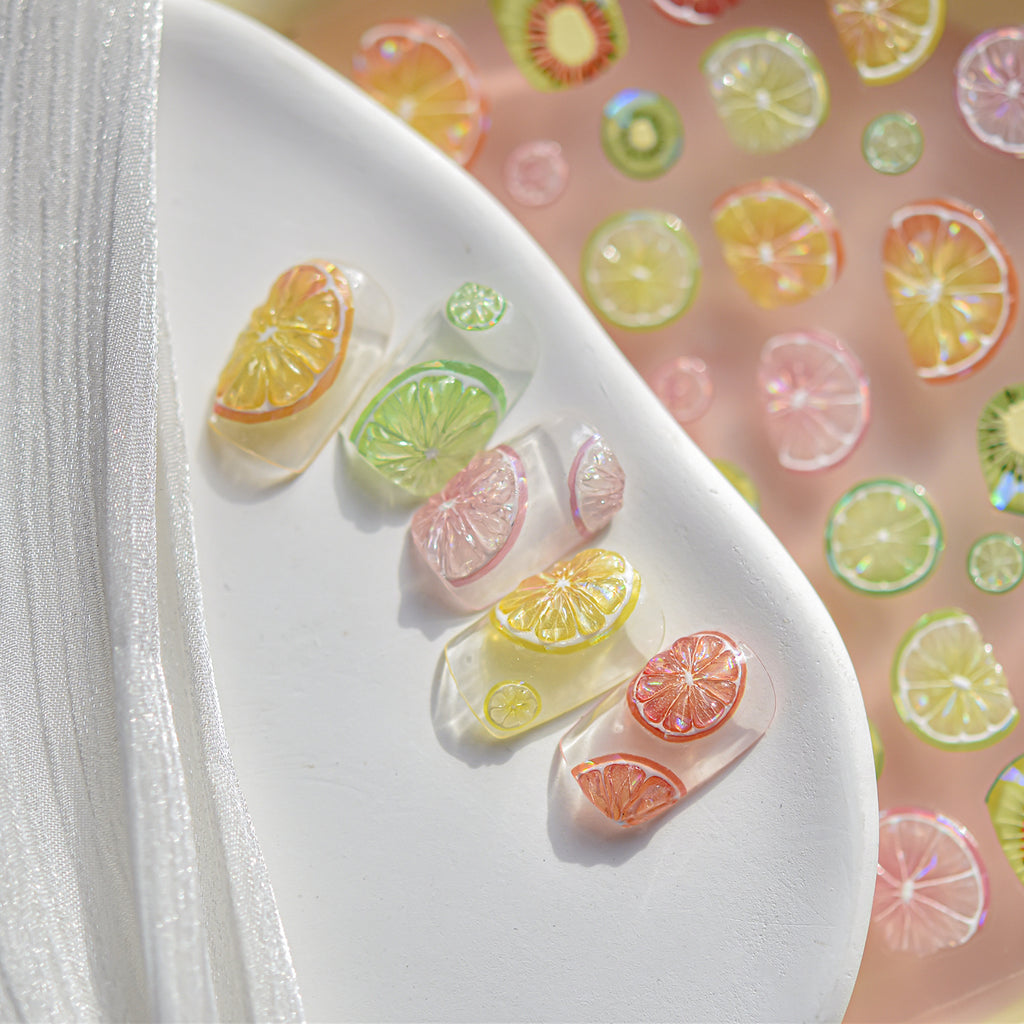 “3D citrus fruit nail art charms applied on clear sample nails, colourful summer nail decoration.”