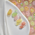 “3D citrus fruit nail art charms applied on clear sample nails, colourful summer nail decoration.”