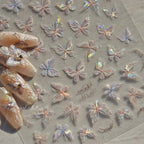 A variety of nail art stickers with butterfly wing designs, featuring glitter and transparent finishes, displayed on a flat surface.