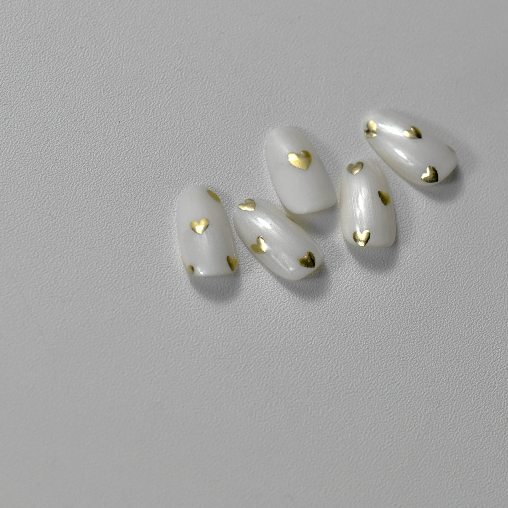 A set of golden metallic hearts  nail art stickers applied on a white nail on a light background.