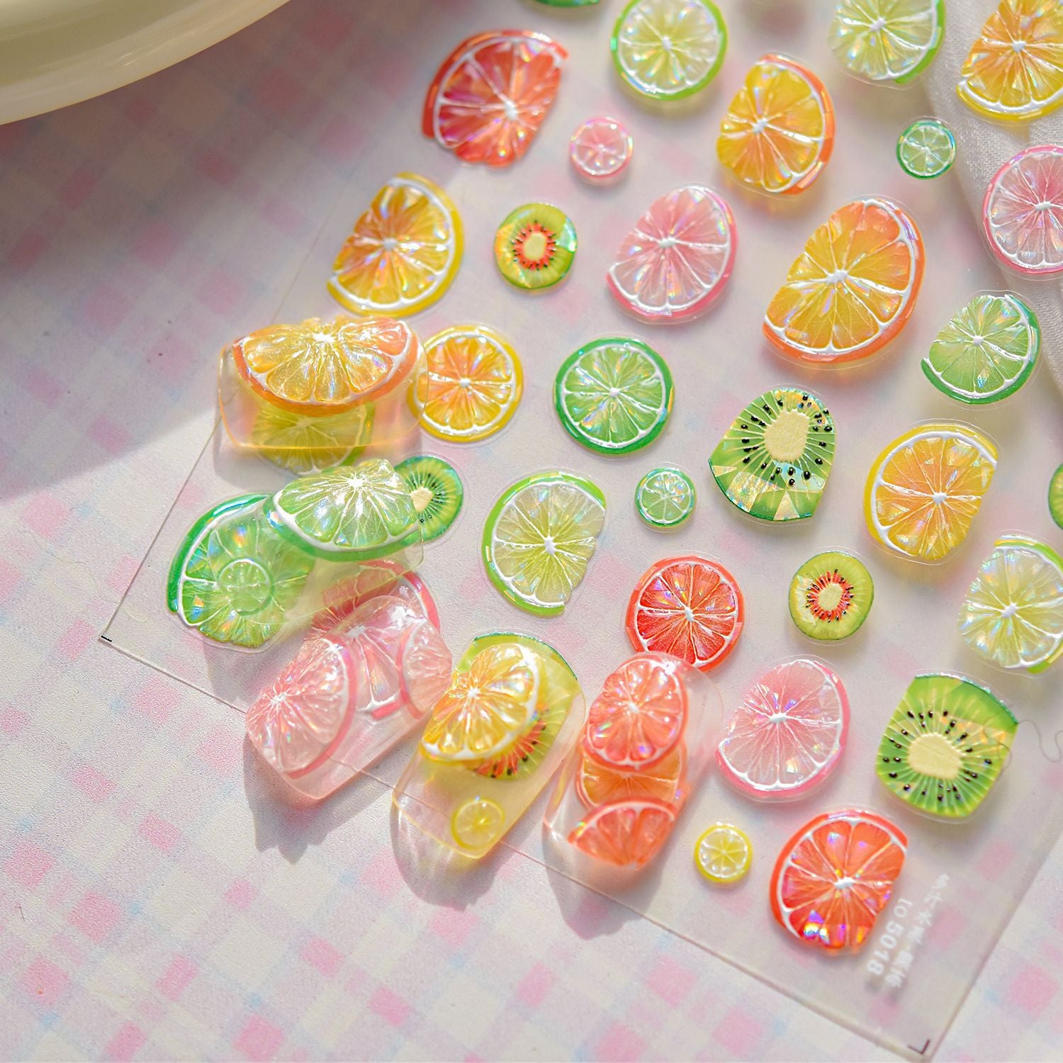 3D fruit nail art stickers with colourful citrus slices and kiwi designs shown with sample nails.