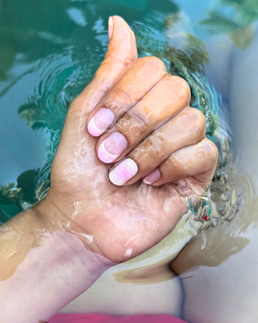 Hand submerged in water showing soft pink gradient  nail wrap manicure on natural nails.