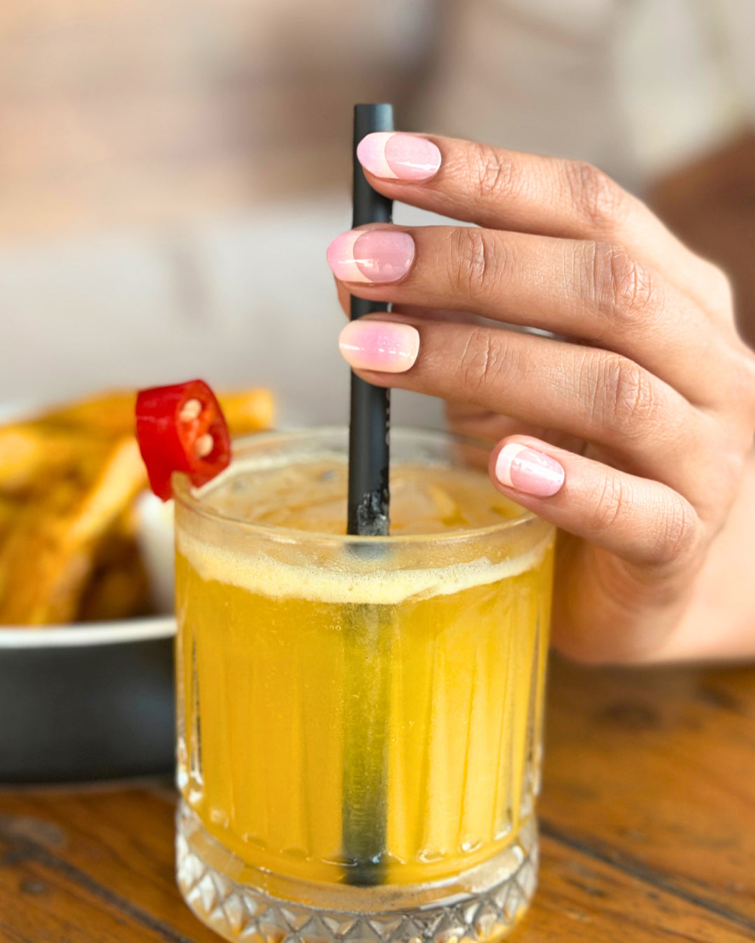 Hand holding a drink with soft pink gradient nail wrap manicure.